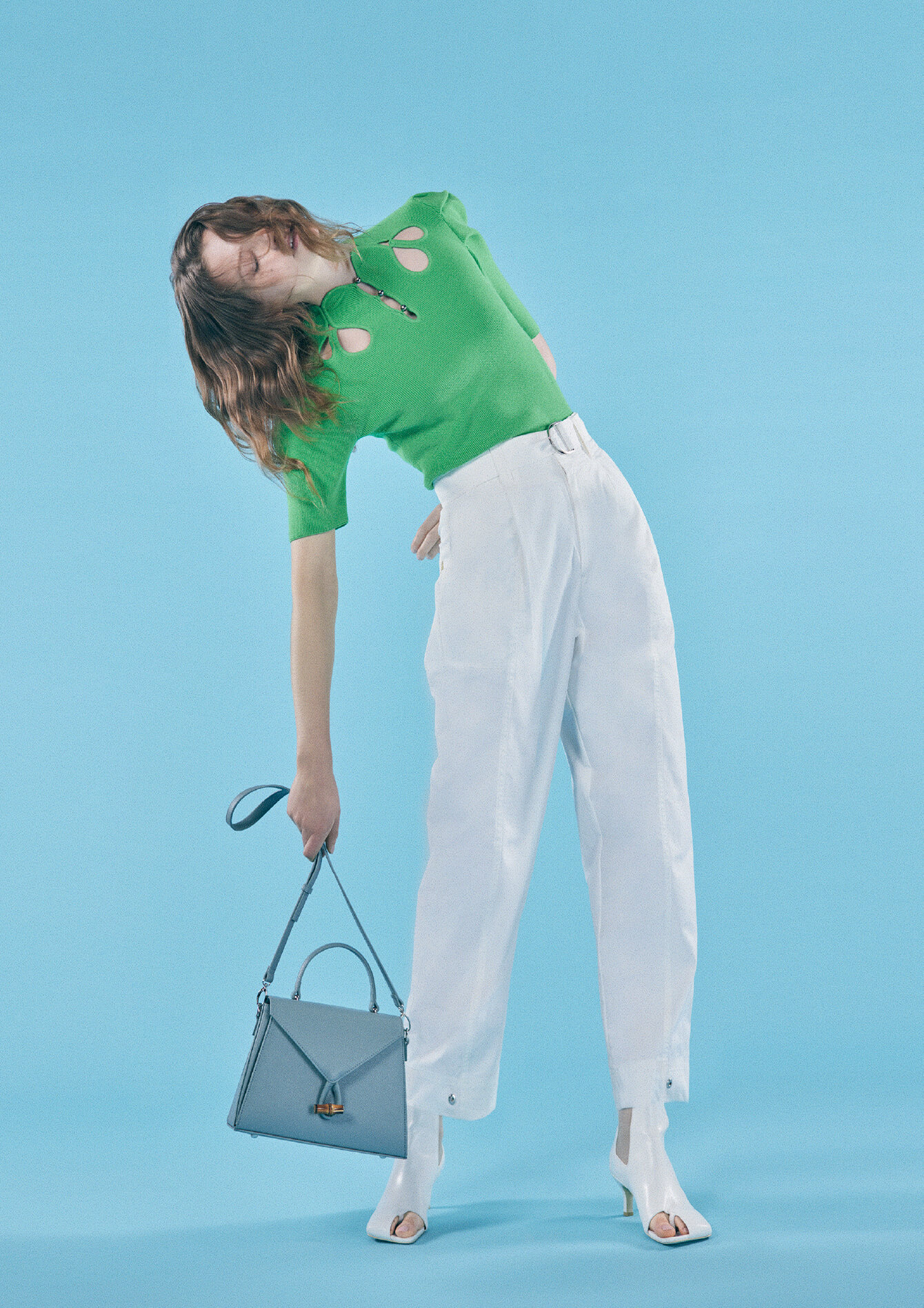 緑色の半袖と白いパンツで青色のカバンを持って上半身を右にそらしている女性モデルの画像