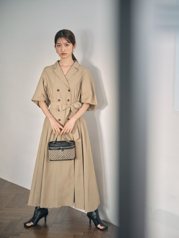 ベージュ色のトレンチコートでカバンを持って正面に向かって立っている女性モデルの画像