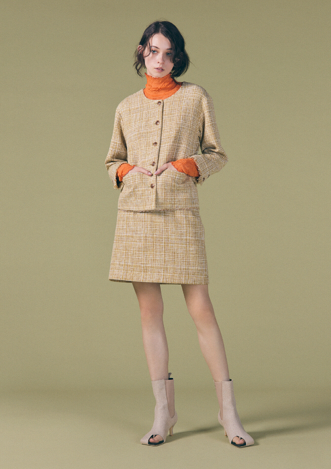 オレンジ色のタートルネックとベージュ色のジャケットとスカートの女性モデルの画像